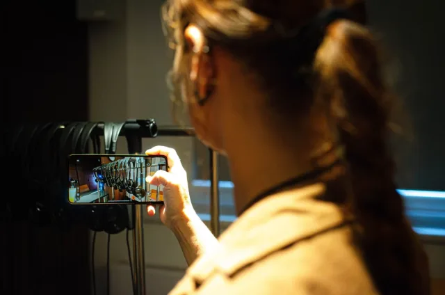 Uczestniczka wizyty fotografuje telefonem stojak ze słuchawkami audioprzewodników.