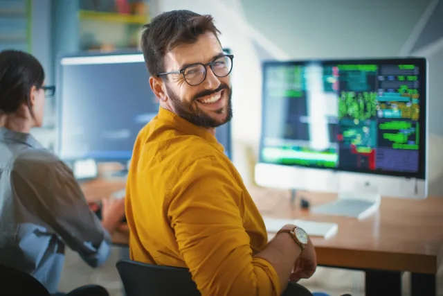 Ilustracja przedstawia uśmiechniętego informatyka.