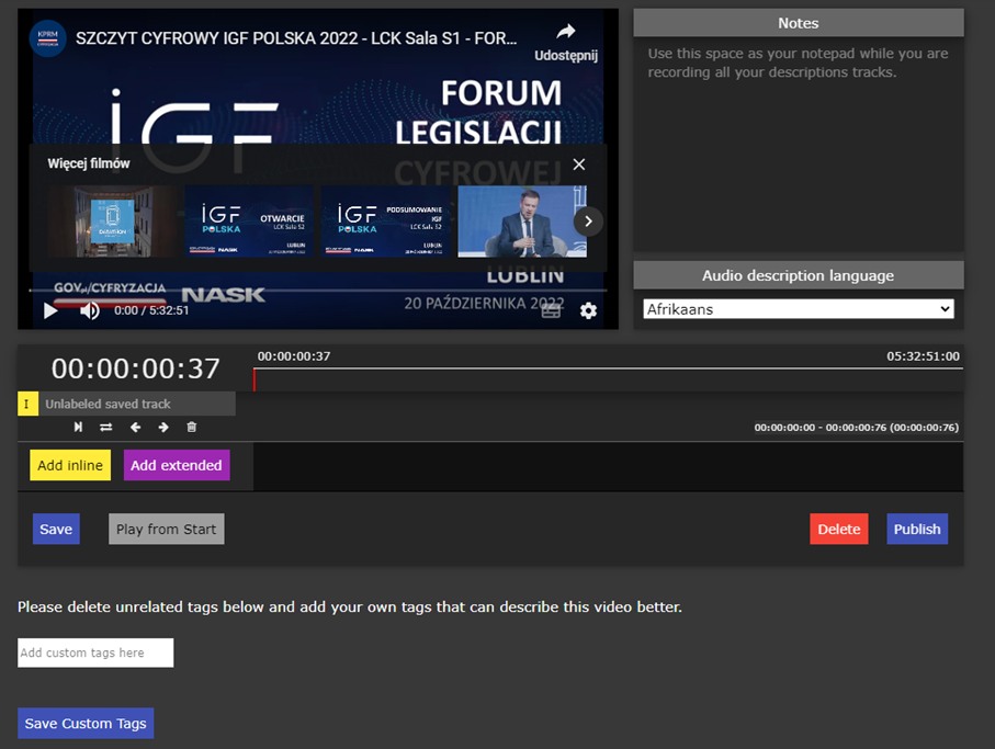 Obraz przedstawia interfejs programu YouDescribe używanego do tworzenia audiodeskrypcji dla filmów. W centrum widoczny jest ekran z odtwarzanym filmem, zatytułowanym „SZCZYT CYFROWY IGF POLSKA 2022 – LCK Sala S1 – FOR...". Pod ekranem znajduje się pasek odtwarzania wideo z zaznaczonym czasem (00:00:37).</p>
<p>Po prawej stronie widoczny jest panel „Notes” z miejscem na notatki oraz opcją wyboru języka audiodeskrypcji (w tym przypadku ustawiony jest język „Afrikaans”).</p>
<p>Pod paskiem odtwarzania znajdują się dwa przyciski do nagrywania audiodeskrypcji: żółty „Add inline” oraz różowy „Add extended”.</p>
<p>Na dole ekranu znajdują się opcje „Save”, „Play from Start”, „Delete” oraz „Publish”. Dodatkowo widoczne jest pole tekstowe do dodawania niestandardowych tagów opisujących wideo oraz przycisk „Save Custom Tags”.